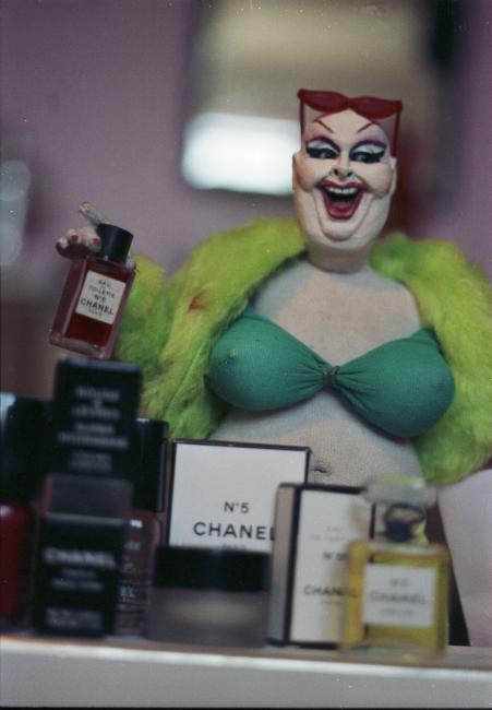 Mattress Factory: Active Archive : Archival Image : Close up of Divine  behind mini Chanel counter, holding up a mini bottle of Chanel perfume,  wearing green cropped outfit [GL.S.2007]